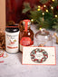 A gift set featuring a bottle of Holiday Honey, a honey pot with dipper, a package of Beekeeper's Tea, and a customizable card, all presented against a holiday-themed backdrop with Christmas lights.